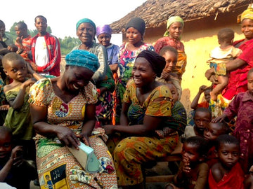 A group of men, women and children from the SPOCADI cooperative community. The women at the front have big smiles.