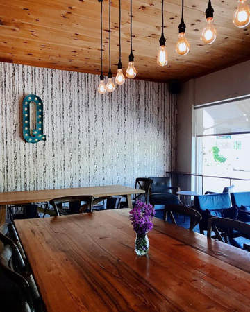 The inside of Quitters cafe with large wooden table, industrial lighting and the letter Q hung on the wall