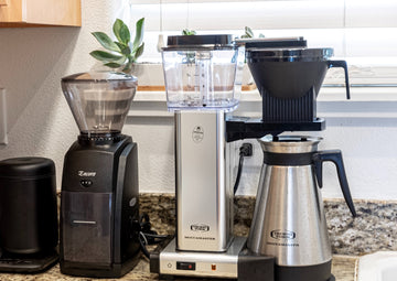 A grinder and coffee maker on a kitchen counter.