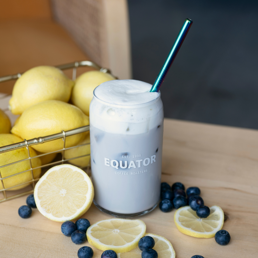 Blueberries and lemons around a drink in an Equator branded glass with a metal reusable straw.