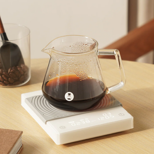 Timemore Basic 2 scale with a coffee server on top and a jar of coffee beans behind and to the left.