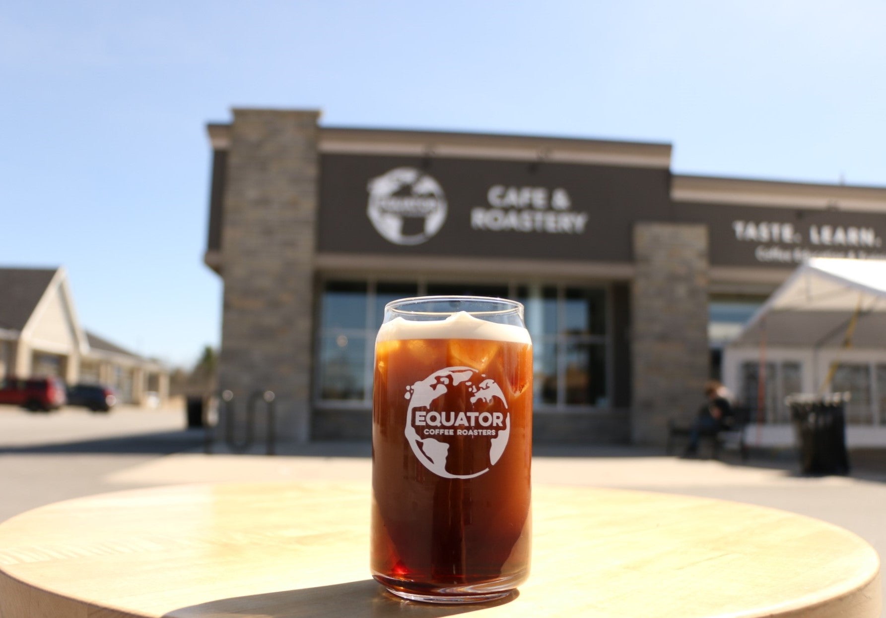 An Equator glass with nitro cold brew and ice in it on a table in the sun.