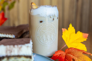 Tiramisu iced latte in a glass with tiramisu cake in the foreground and background (both blurred) and with some yellow and orange leaves.