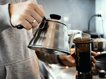 A person pouring hot water from a kettle into an Aeropress.
