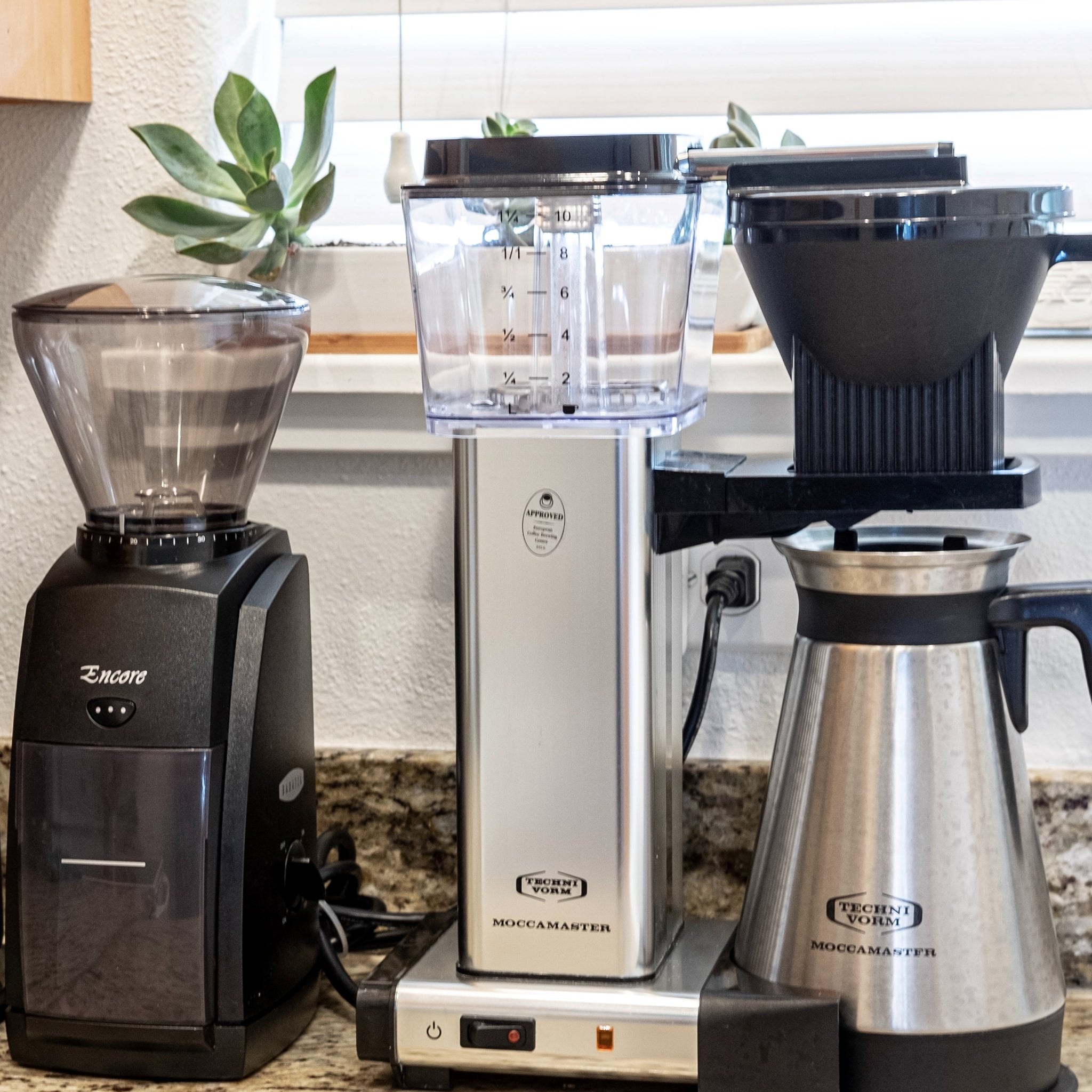 A grinder and coffee maker on a kitchen counter.