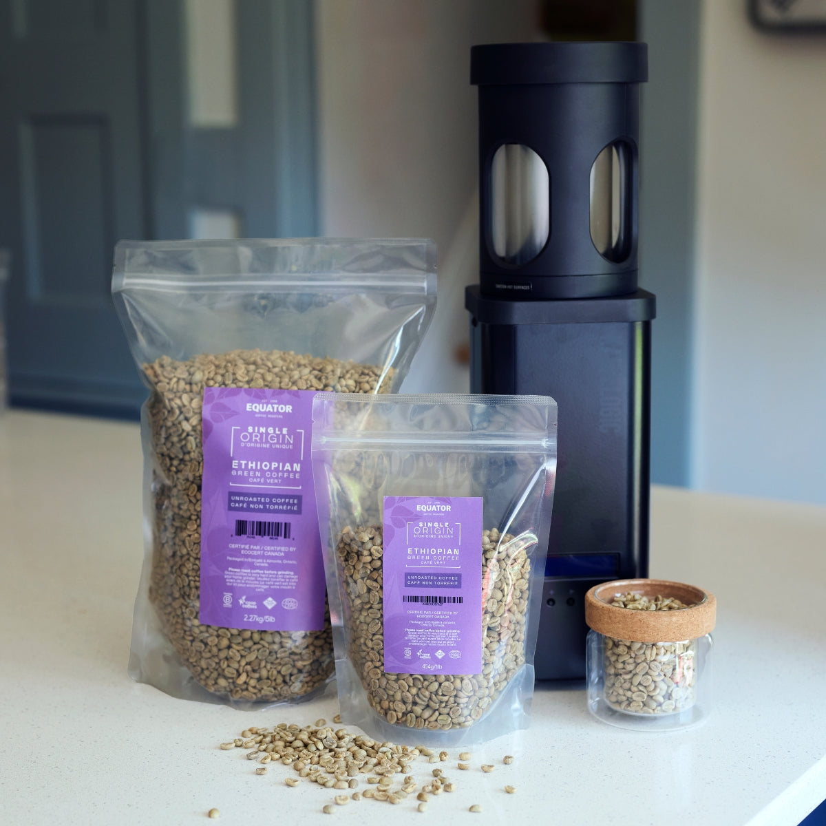 1lb and 5lb packages of green coffee beans from Ethiopia beside a black home coffee roaster.