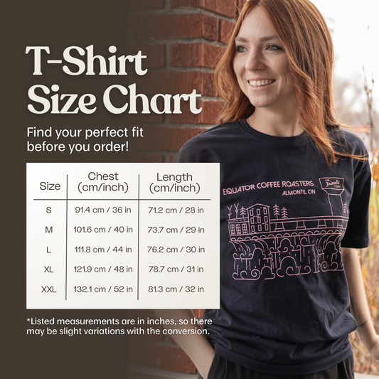 Person wearing a navy t-shirt with the Almonte design, standing in front of a brick wall, with a size chart overlay.