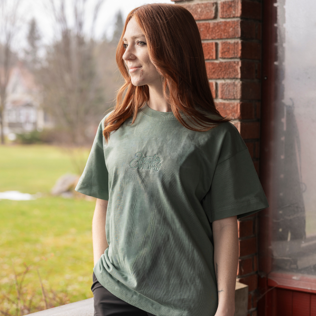 Person wearing a green t-shirt in front of a brick wall.
