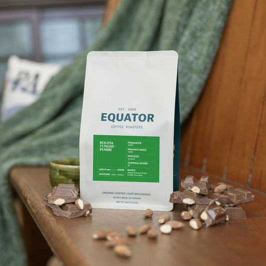 Bag of Bolivia Yungas-Pumiri single origin on a bench with chocolate and almonds and a blanket in behind.