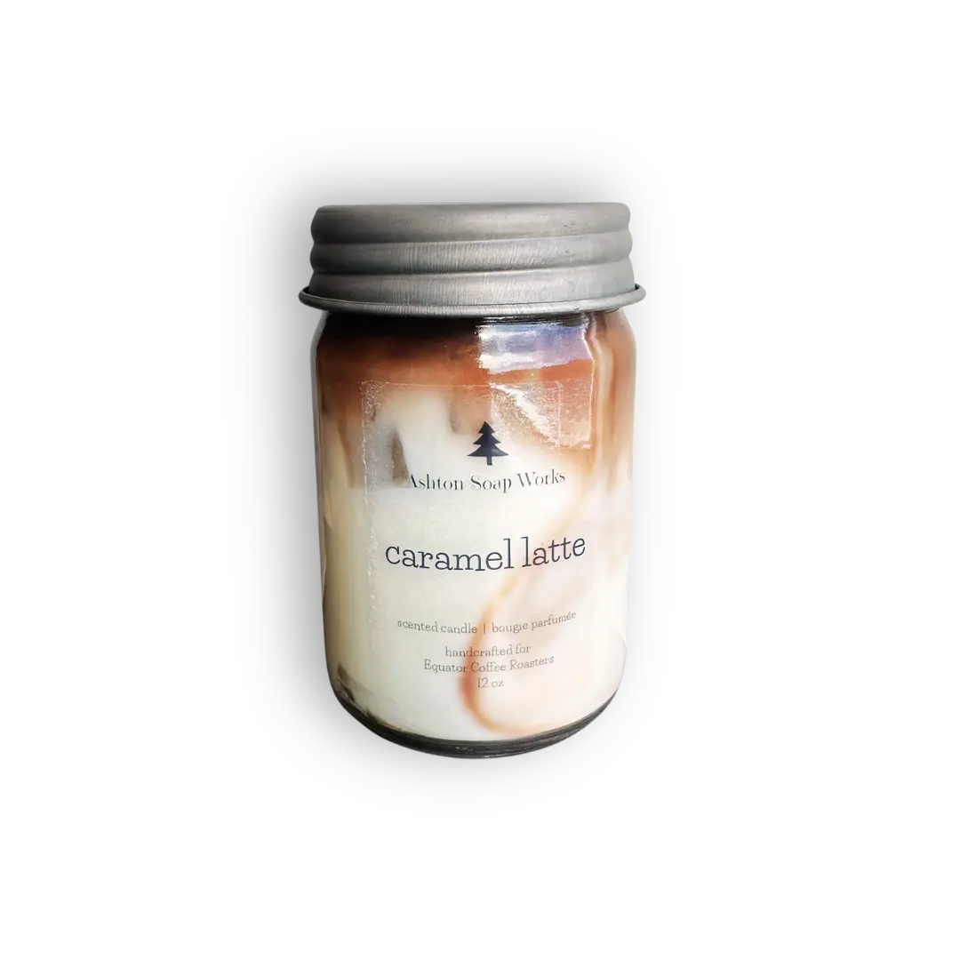 Hand poured candle in a clear glass mason jar with a silver metal lid, featuring a 'caramel latte' scent by Ashton Soap Works. The wax is swirled with brown and cream tones, visible through the clear glass.
