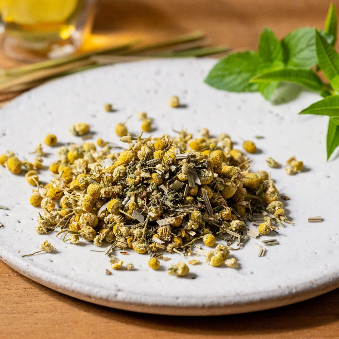 Chamomile Medley loose leaf tea on a white plate with a glass of tea and mint leaves in the background