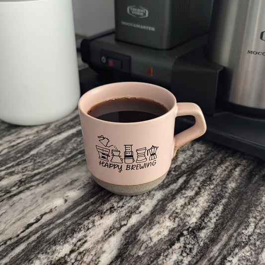 Rustic pink ceramic mug with coffee in front of a coffee maker.