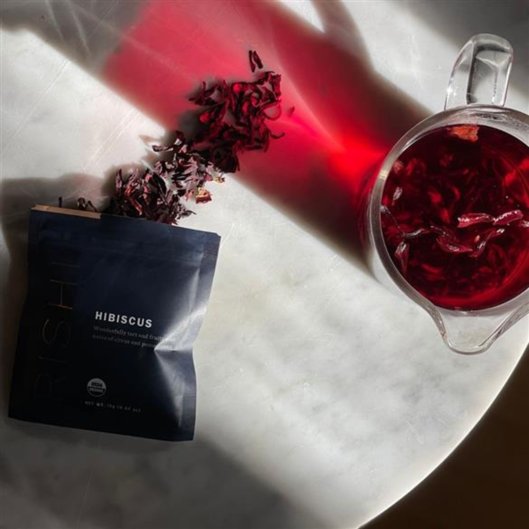 A package with hibiscus loose leaf tea spilled out and a pitcher of iced hibiscus tea.