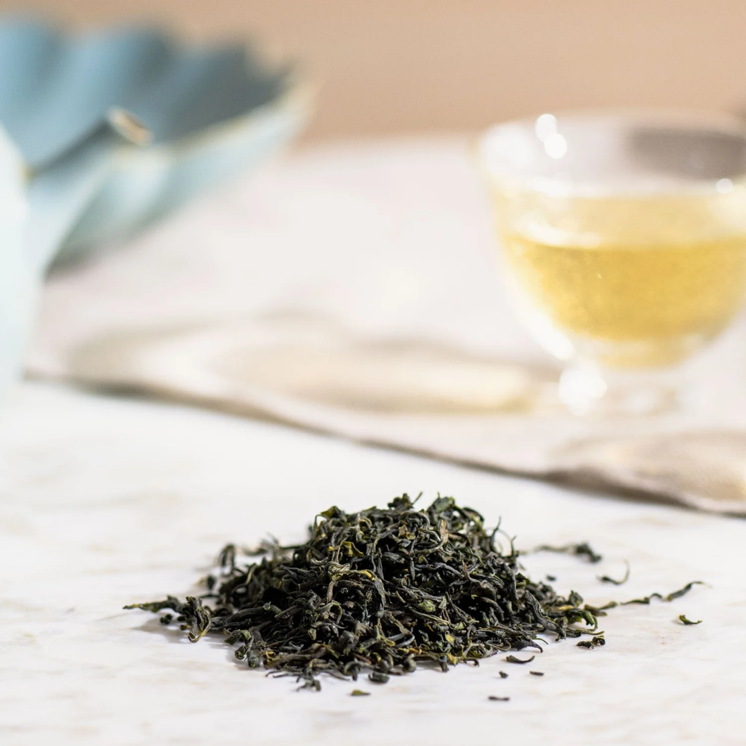 Jade Cloud tea leaves on a counter with a blurred glass of tea in the background.