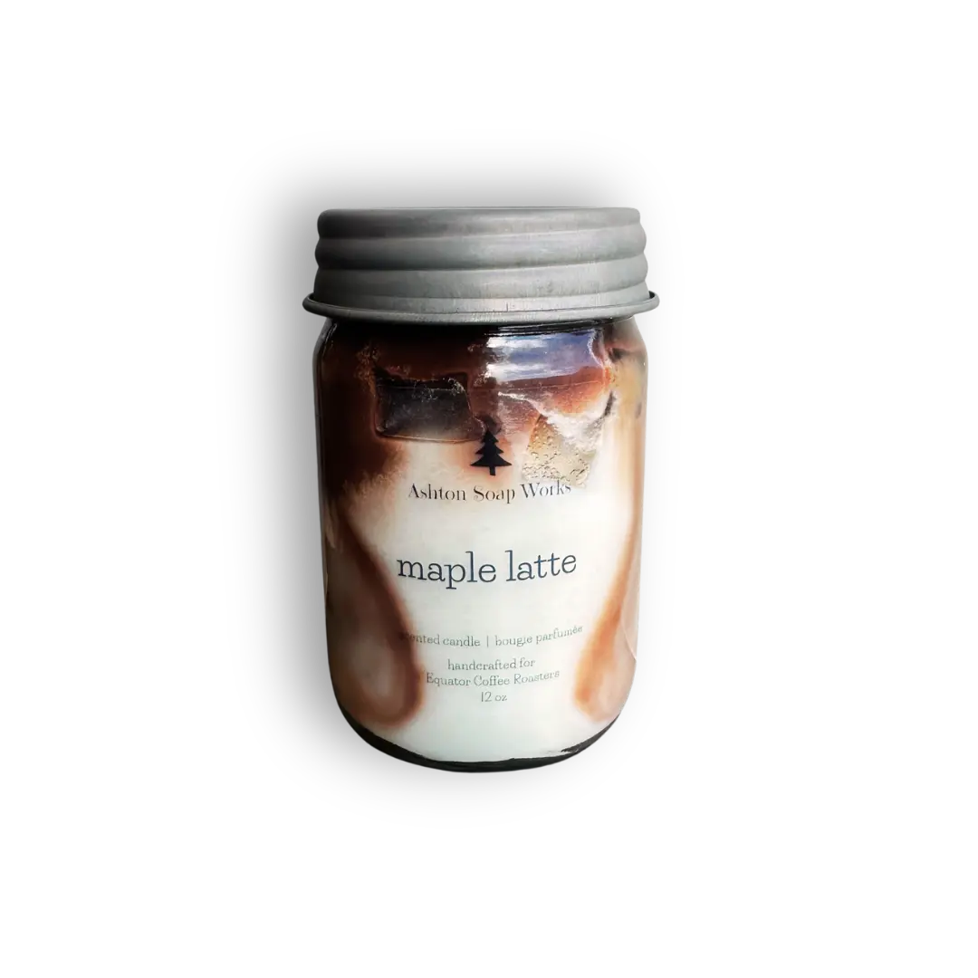 Hand poured candle in a clear glass mason jar with a silver metal lid, featuring a 'maple latte' scent by Ashton Soap Works. The wax is swirled with brown and cream tones, visible through the clear glass.