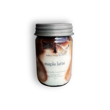 Hand poured candle in a clear glass mason jar with a silver metal lid, featuring a 'maple latte' scent by Ashton Soap Works. The wax is swirled with brown and cream tones, visible through the clear glass.