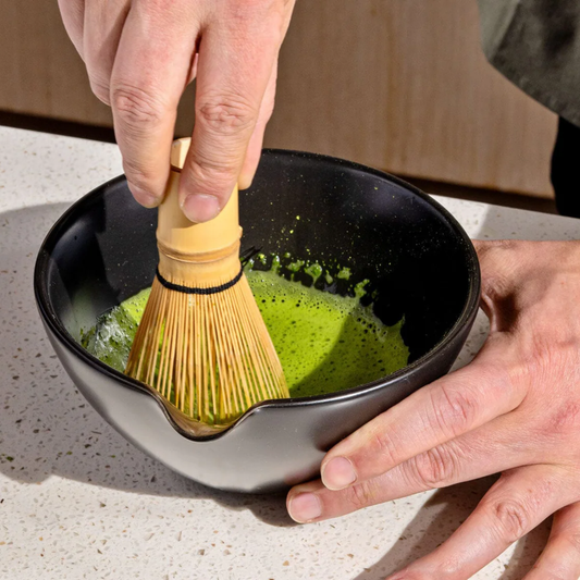 Person using a Rishi bamboo whisk to stir green tea in a Rishi pouring bowl.
