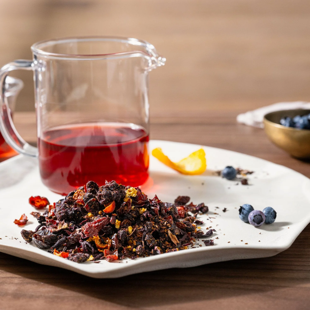 Scarlet Tea leaves on a plate with a glass of steeped tea and a lemon peel and blueberries.