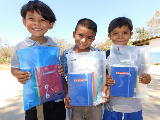 Three children holding school supplies given to them by SchoolBox.